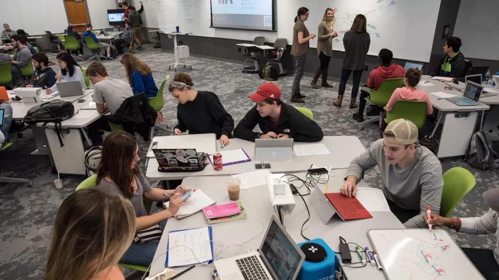 Students and Faculty in the TILL classroom conversing and working together on laptops