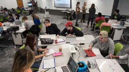 Students and Faculty in the TILL classroom conversing and working together on laptops